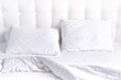 Soft white quilted pillow and blanket coverlet in bed on the background of white leather quilted headboard. Clean pillow, part of bed close-up, comfort. Quilted headboard background, bedding mockup
