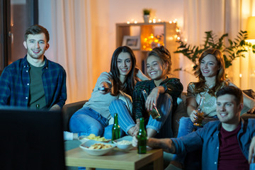 Poster - friendship, and leisure concept - happy friends with non-alcoholic drinks and snacks watching tv at home in evening