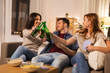 © Syda Productions - friendship, leisure and entertainment concept - happy friends playing cards game and clinking beer bottles at home in evening