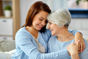 family, generation and people concept - happy smiling senior mother with adult daughter hugging at home