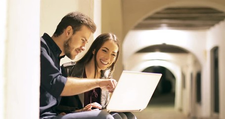 Sticker - Happy couple browsing laptop content sitting in a town street in the night