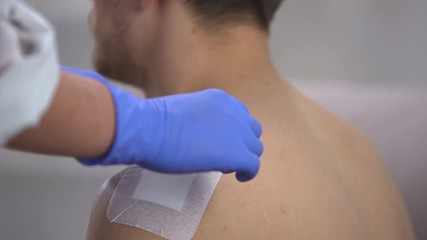 Wall Mural - Nurse hands taking off adhesive bandage from scratched shoulder of male patient