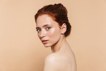 Wall Mural - young redhead woman posing isolated over beige wall background.