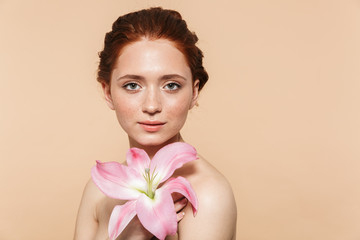 Wall Mural - pretty young redhead woman posing isolated over beige wall background pink flower.