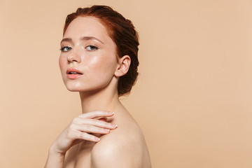 Wall Mural - young redhead woman posing isolated over beige wall background.