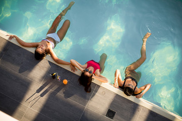 Wall Mural - Three beautiful slim women in bikini relaxing and drink cocktails on poolside of a swimming pool