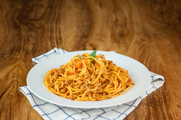 Spaghetti with tomato sauce in a white plate on a wooden background.