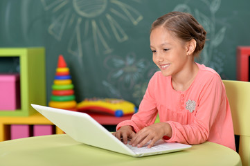 Sticker - Portrait of emotional little girl using laptop while sitting at desk in classroom