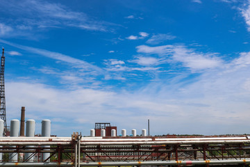 Wall Mural - View of a pipeline overpass with pipes, columns of tanks against a blue sky with clouds at an industrial chemical refinery petrochemical plant