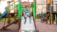 Photo Of Adorable Smiling Boy Climbing And Riding On Slide. Active Child Having Fun And Playing At Park
