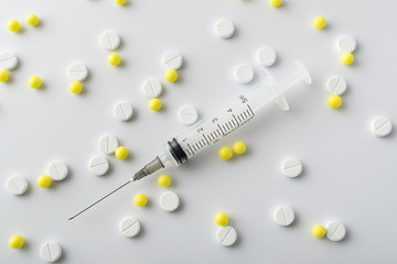 Wall Mural - medical syringe next to yellow and white pills of medical drugs and vitamins are in the hospital on a white background