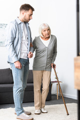 Sticker - full length view of man helping senior mother with cane at home