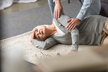 Cropped View Of Man Helping Senior Mother With Heart Attack Fallen On Carpet