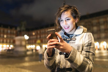 Spain, Madrid, Plaza Mayor, Happy Young Woman Using Her Smartphone
