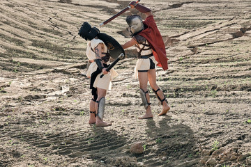 A concept photo of a Roman battle of two warriors of the Colosseum in action with aggressive emotions in full military uniform on a desert landscape on a sunny day with a dry sun.