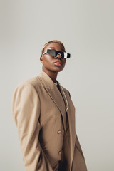 fashionable african american girl posing in sunglasses and beige jacket isolated on grey