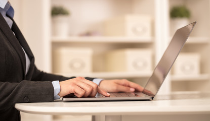 Business woman below chest working on her laptop in a cozy environment
