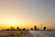 Golden Beautiful Sunrise Clear With Dry Grass Fields And Long Asphalt Road & Electric Pole In The Countryside At Morning On Quiet Day