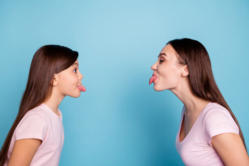 Poster - Close-up profile side view portrait of two nice attractive charming foolish childish cheerful straight-haired girls showing tongue out isolated over bright vivid shine green blue turquoise background