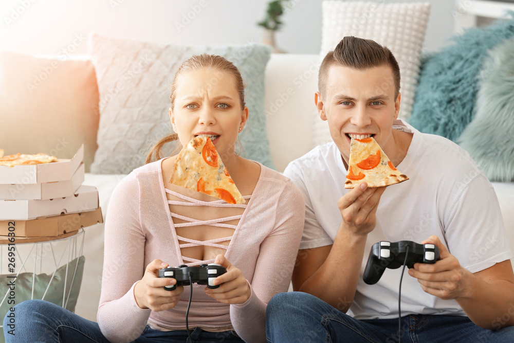 Young couple eating tasty pizza while playing video games at home