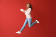 Jumping young woman with books on color background