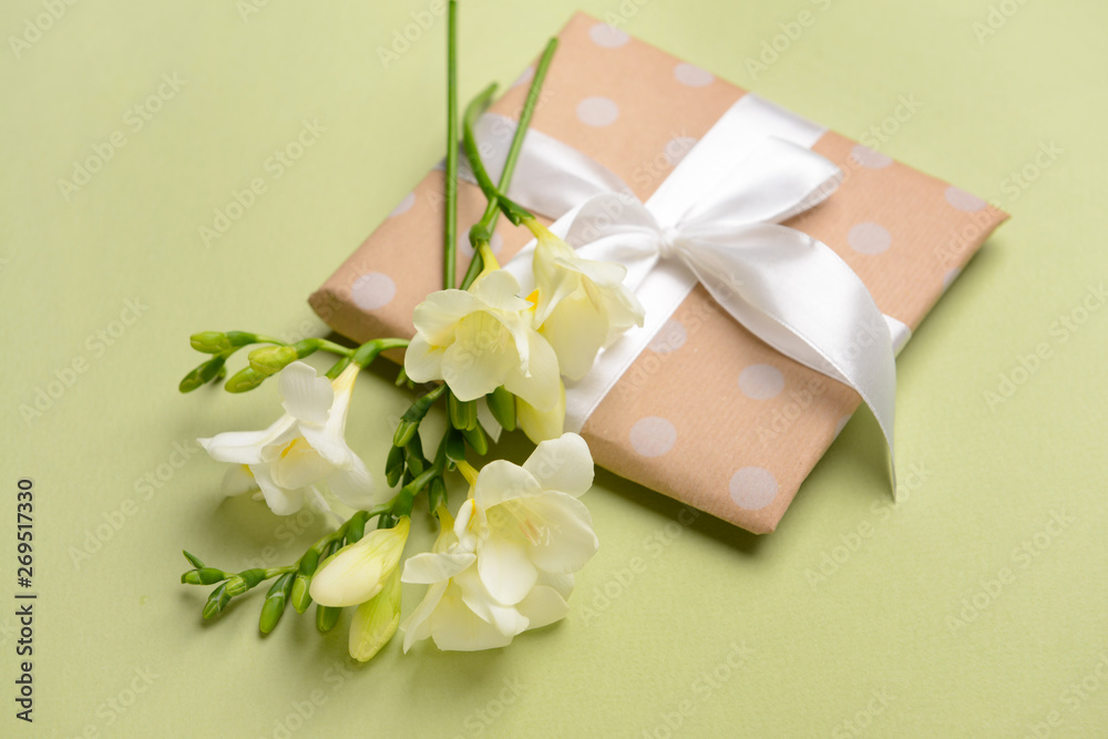 Beautiful freesia flowers and gift on color background