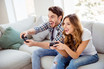 Portrait of his he her she two person nice attractive lovely cheerful cheery positive glad guy lady sitting on divan playing station having fun in light white style interior hotel house indoors