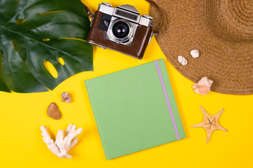 Women's traveler accessories: coral, shell, starfish, straw hat, tropical leaf monstera, retro camera, notebook with copy space on yellow background. Summer concept of travel background