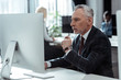 © LIGHTFIELD STUDIOS - selective focus of pensive mature businessman holding glasses and looking at computer monitor near multicultural colleagues in office