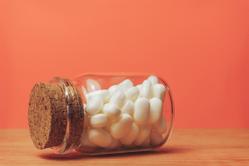 Poster - Glass bottle for pills on a red wood table. Beautiful corall orange background.
