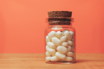 Poster - Glass bottle for pills on a red wood table. Beautiful corall orange background.