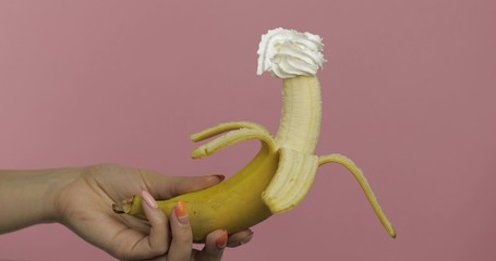 Woman hand holds banana with whipped cream on top of the fruit