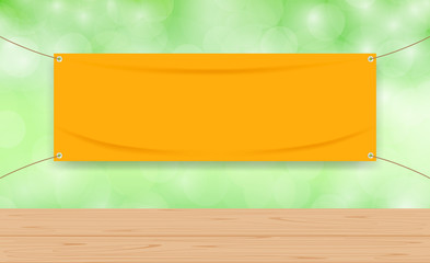 Wall Mural - vinyl blank orange on green bokeh background and wood plank table, mock up textile fabric empty of banner advertising stand hanging, indoor outdoor fabric vinyl backdrop for copy space presentation ad