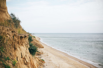 Beautiful sandy cliff with grass and sea waves on beach with on tropical island. Big rock and waves in ocean bay or lagoon. Tranquil calm moment. Summer vacation. Copy space