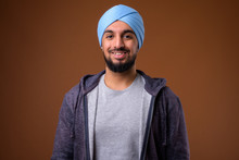 Young Bearded Indian Sikh Man Wearing Turban Against Brown Backg