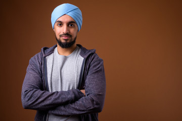 Wall Mural - Young bearded Indian Sikh man wearing turban against brown backg