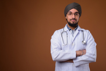 Wall Mural - Young bearded Indian Sikh man doctor wearing turban against brow