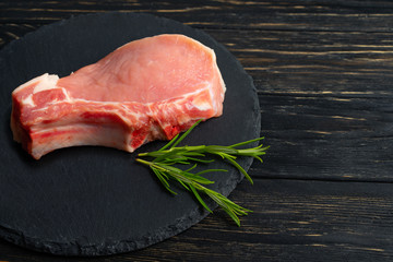 Top view of one pieces raw pork chop steaks with rosemary on a black stone cutting board.