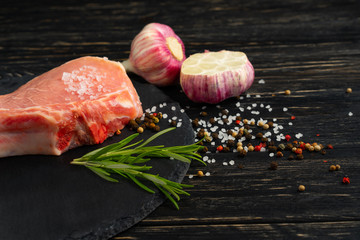 Top view of one pieces raw pork chop steaks with on a black stone cutting board.