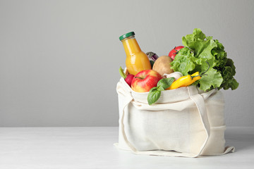 cloth bag with vegetables and bottle of juice on table against grey background. space for text
