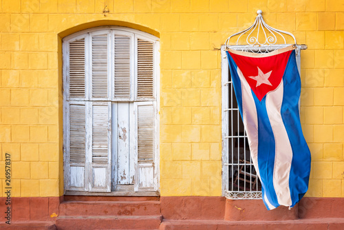Obraz na plátně  Cuban flag hanging at the window of a colorful house in a street of Trinidad, Cu