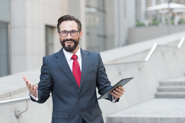 Cheerful shot of smiling manager standing outdoors with a tablet in hand