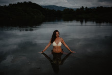 Young Woman In Swimwear Standing In Calm Water Of Pond In Evening In Nature