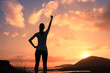 silhouette of young strong victorious woman with fist in the air at sunset