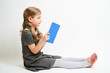 © briagin - Little girl photographed against white background wearing school uniform dress isolated sitting with open blue book
