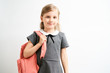 © briagin - Little girl photographed against white background wearing school uniform dress isolated holding a coral backpack on one shoulder
