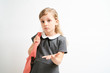 © briagin - Little girl photographed against white background wearing school uniform dress isolated holding a coral backpack on one shoulder