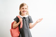 © briagin - Little girl photographed against white background wearing school uniform dress isolated holding a coral backpack on one shoulder