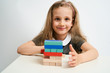 © briagin - Little girl photographed against white background wearing school uniform dress isolated playing jenga