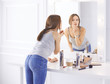 © lenetsnikolai - Amazing young woman doing her makeup in front of mirror. Portrait of beautiful girl near cosmetic table
